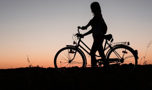 一人夕焼けをバックに自転車を押している女性