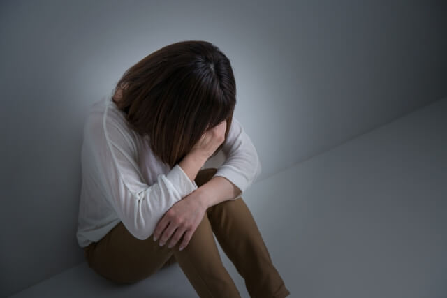 膝を抱えて悩んでいる女性