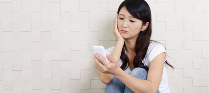 スマホを見ながら悩んでる女性